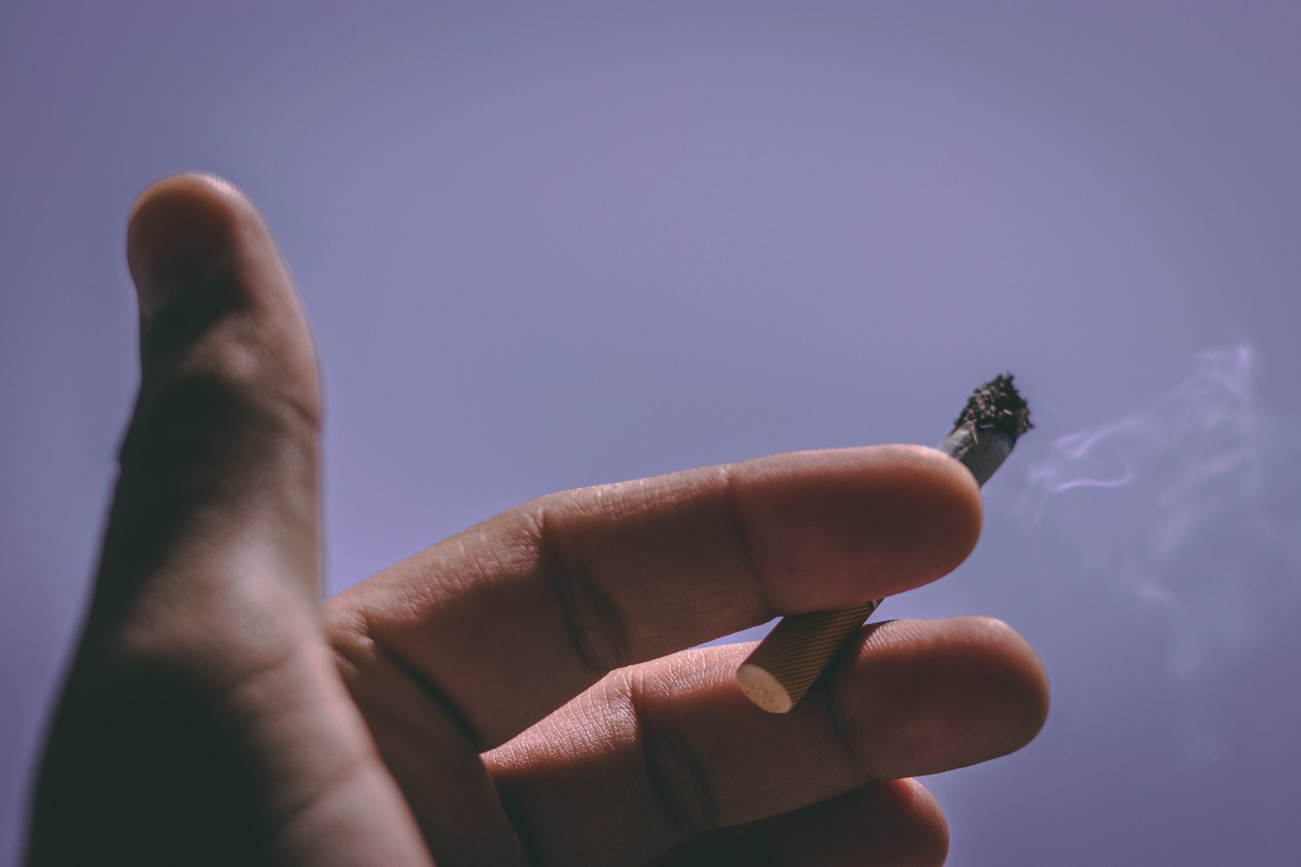 Ozonowanie usuwa nieprzyjemne zapachy dymu papierosowego - na obrazku widać rękę z papierosem pomiędzy palcami na tle fioletowego nieba